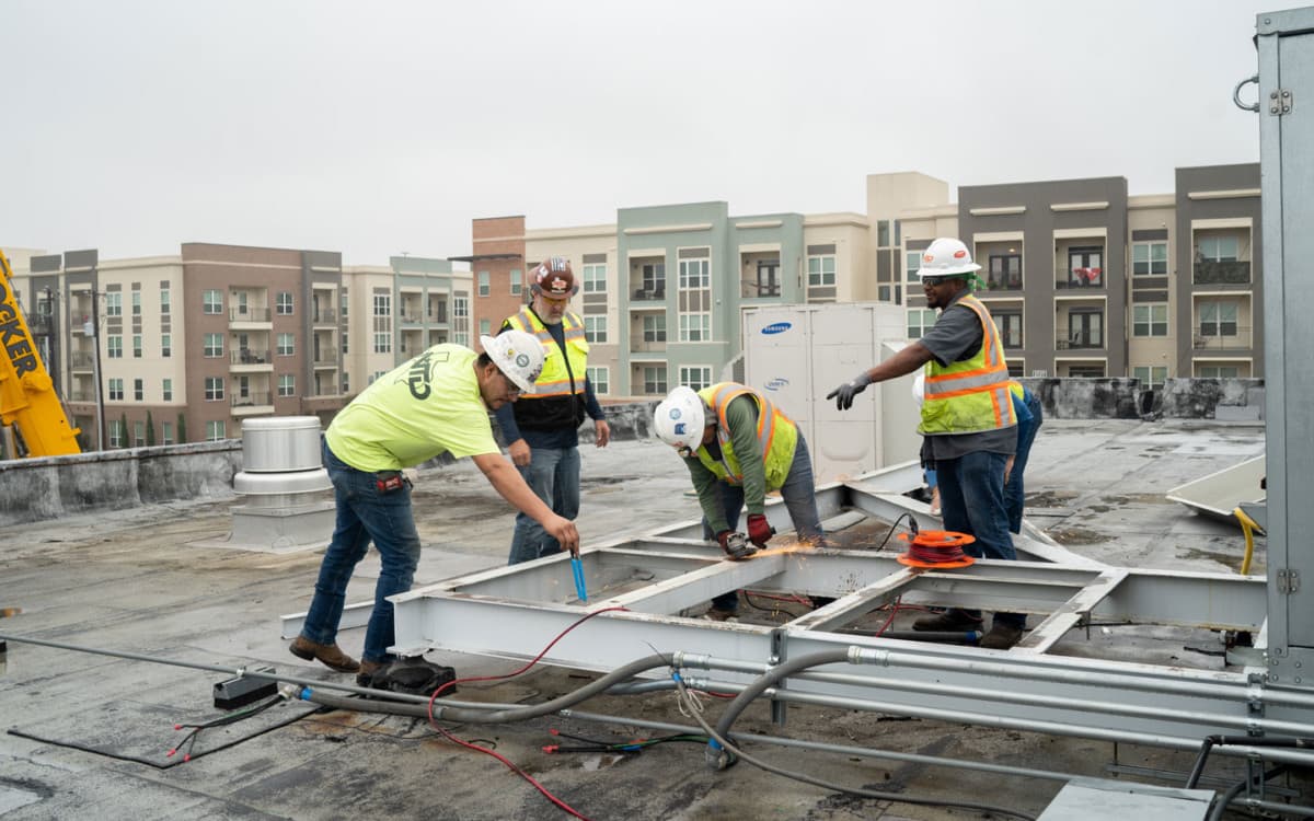 Workers grinding and welding HVAC curb adapter on commercial rooftop