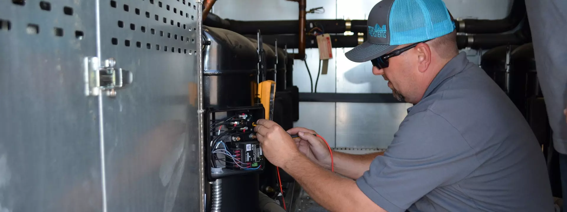 Technician with multimeter testing wiring on HVAC compressor unit