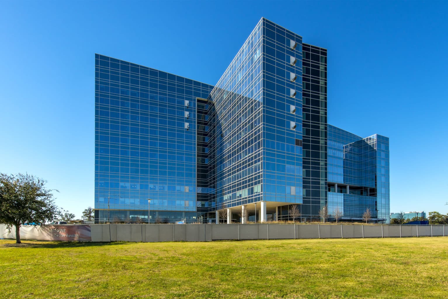 Modern glass corporate campus building with green lawn and blue sky