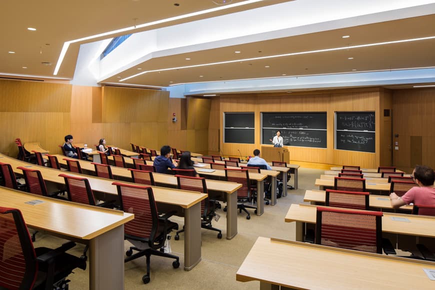 Tiered university lecture hall with wood paneling, recessed lighting, and modern HVAC ceiling design