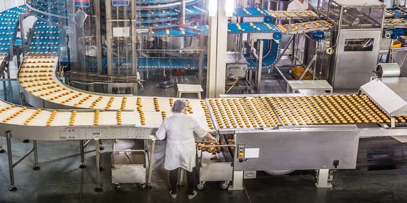 Bakery production line with curved conveyor belt and worker in hairnet and white coat