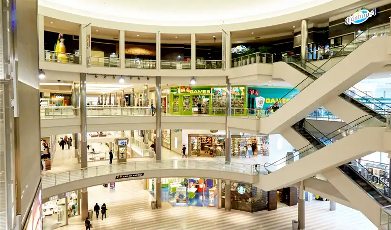 Multi-level shopping mall atrium with escalators, glass railings, and retail storefronts